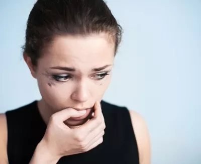 A woman with tear-streaked makeup looks anxiously away, biting her nails in a gesture of worry.