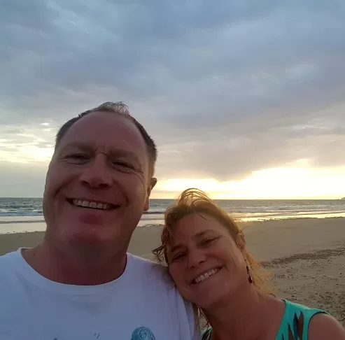 A smiling couple takes a close-up selfie on the beach with the sunset in the background, creating a warm and joyful atmosphere.